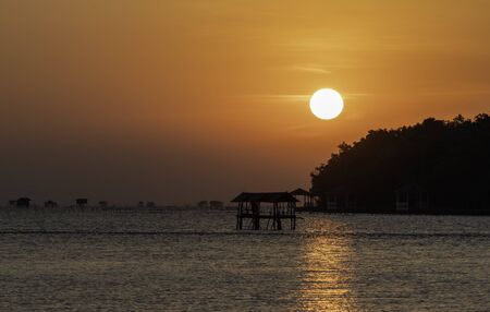 Sunrise from the sea with Silhouette old hut in the seaの写真素材