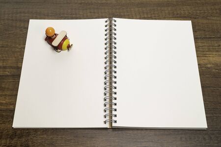 Red and yellow wooden airplane toy on white blank notebook on wooden tableの写真素材