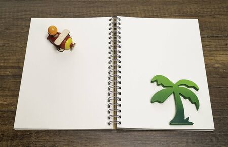 Red and yellow wooden airplane on blank white notebook with green palm treeの写真素材