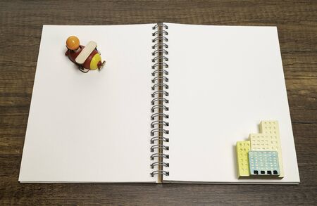 Red wooden airplane on blank white notebook with ceramic building toyの写真素材