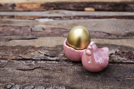 Decorative dyed golden easter eggs in pink glossy ceramic decoration with hen on dark brown wooden...