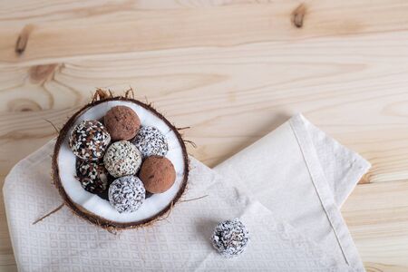 Raw protein energy balls with nuts, dried fruits and honey in the half of coconut on napkin. Light wooden background. Coconut bowl. Copy space, top viewの写真素材