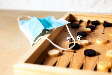 Board game, wooden backgammon and a medical mask on light background, the concept of leisure during the quarantine. Close upの写真素材
