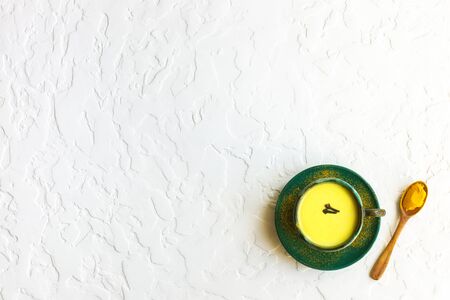 Turmeric golden milk latte with spices. Ceramic cup with indian beverage and wooden spoon with turmeric on white background. Detox healthy cozy drink. Top view, copy space, horizontalの写真素材
