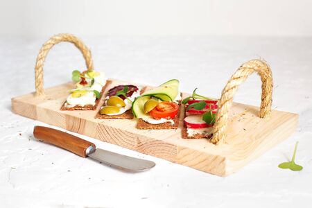 Rye bread sandwiches with curd cheese, vegetables and microgreen on wooden tray