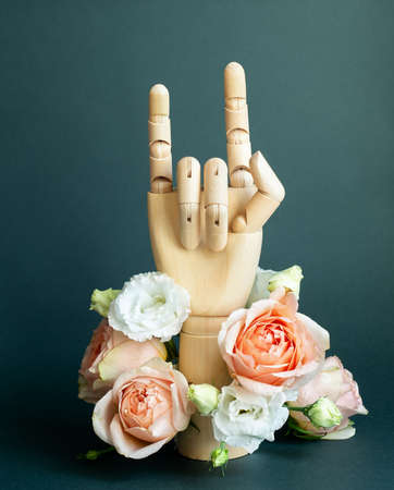 Wooden hand making Devils horns with flowers on dark green backgroundの写真素材