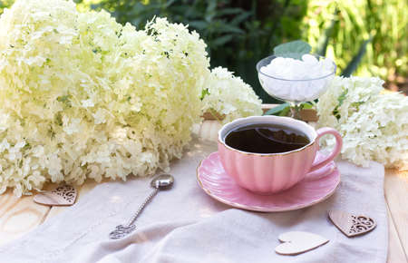 Composition with cup of black tea, sugar in bowl and white hydrangea flowers on rustic napkin on the wooden tableの写真素材