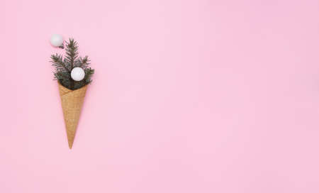 Ice cream cone with christmas tree branche and white baubles on pink background. holiday concept. Horizontal banner with creative new year holiday concept. Flat lay, copy space, top view.の写真素材