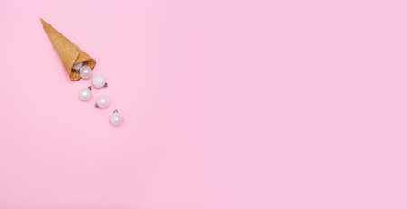 White glitter Christmas decoration baubles roll out of ice cream cone on pastel pink background. Creative new year concept with copy space. Horizontal banner with flat lay. Top view, place for textの写真素材