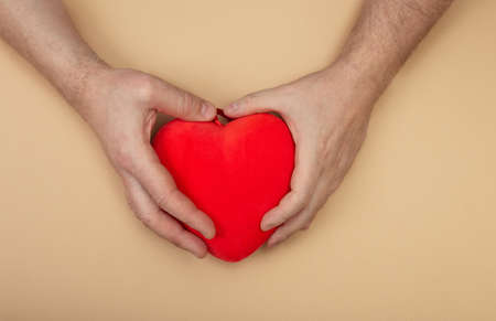 LGBT concept with men hands holding red heart on beige background. Hands of homosexual couple on set...