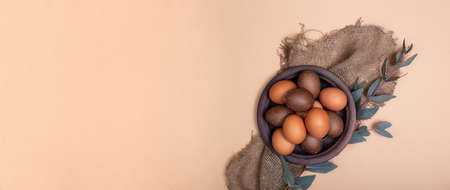 Horizontal banner with clay plate full of painted Eastr eggs on sustainable burlap cloth with...