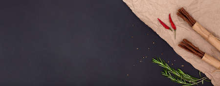 Horizontal banner with dried meat sticks, red pepper and rosemary on craft paper on black background...