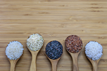 Variety of rice in wood spoon on wood background. From left: Japanese rice, pounded brown rice, forbidden rice (riceberry), pounded red rice, jasmine riceの写真素材