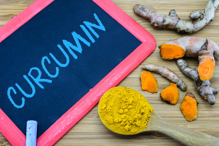 Curcumin  written on chalkboard with turmeric powder and turmeric root on wood background