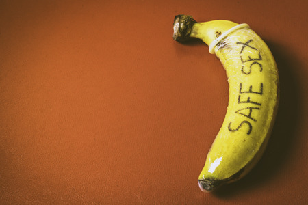 Safe sex concept of condom on banana with red backgroundの写真素材