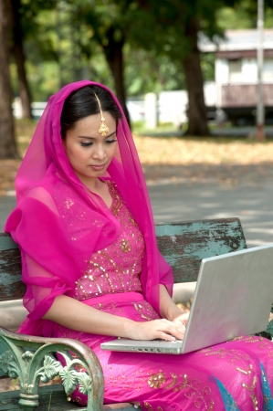 Pretty Asian in pink Indian clothes working on laptop の写真素材