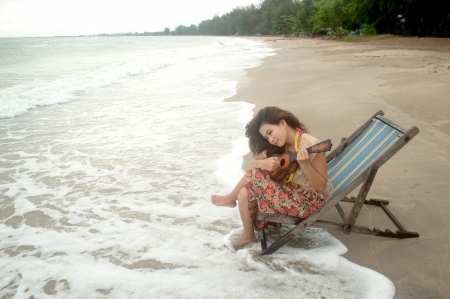 Pretty Asian woman playing ukulele on beach bed  の写真素材