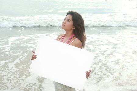 Beautiful Asian woman holding a white billboard on the beach  の写真素材