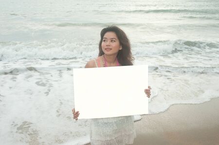 Beautiful Asian woman holding a white billboard on the beach  の写真素材