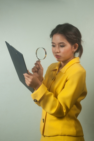 Pretty young Asian business woman looking document by magnifying glass の写真素材