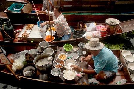 Ratchaburi, Thailand - July 21, 2013   Senior Thai woman and male selling noodle freshly cooked food on her boat in Damnuan Saduak Floating Market,Ratchaburi Province in Middle of Thailand のeditorial素材