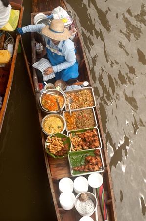 Ratchaburi, Thailand - July 21, 2013   Senior Thai woman selling freshly cooked food and fruits on a boat in Damnuan Saduak Floating Market,Ratchaburi Province in Middle of Thailand のeditorial素材