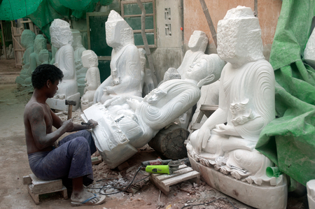 Burmese man use tool carving a large marble Buddha statue, outdoors. Man is surrounded with several other statues in Mandalay city,Central of Myanmar.のeditorial素材