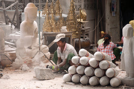 Burmese man use tool carving a large marble Buddha statue, outdoors. Man is surrounded with several other statues in Mandalay city,Central of Myanmar.のeditorial素材