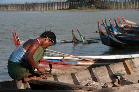 Man repair traditional boat on the shore of the Taungthaman lake near U-Bein Bridge.のeditorial素材