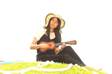 Pretty young asian woman sitting on grass holding Ukuleleの写真素材