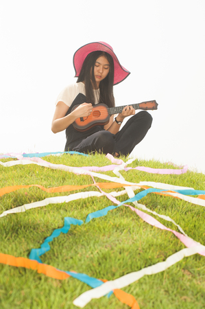 Pretty young asian woman sitting on grass holding Ukuleleの写真素材