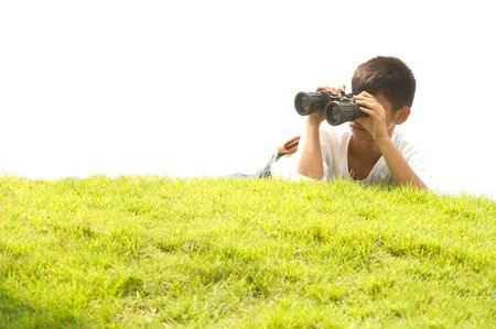 Asian young boy lying on grass using binoculars.の写真素材
