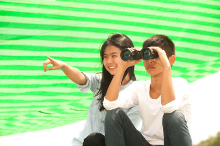 Asian young boy and girl sitting on grass using binoculars .の写真素材