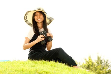 Pretty Asian young  woman sitting on grass using binoculars .の写真素材