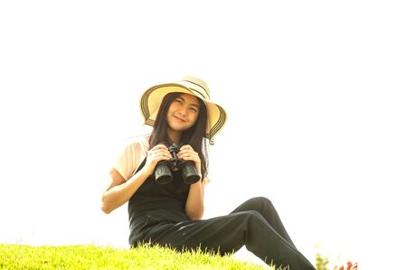 Pretty Asian young  woman sitting on grass using binoculars .の写真素材