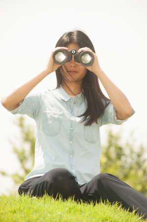 Pretty Asian young  woman sitting on grass using binoculars .の写真素材
