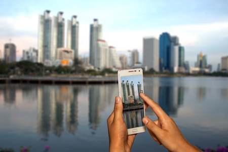 Hand of photographer with smart phone shooting image on blurred Building of Bangkok city background.の写真素材