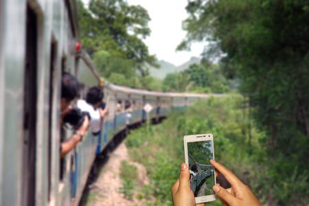 Hand of photographer with smart phone shooting image on blurred tourist on train background.の写真素材
