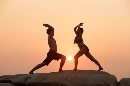 Couple are engaged in fitness yoga exercise on the stone in Sunset.の写真素材