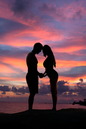 Lovely young adult couple standing on the rocks above tropical sea in Sunset.の写真素材