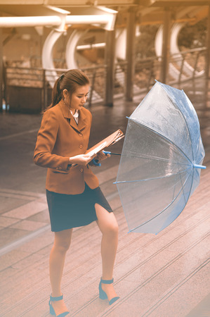 Thai pretty woman in red office suit holding transparent umbrella walking on bridge crossing landmark in Bangkok,Thailand.の写真素材