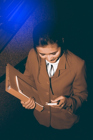 Asian Pretty woman in red suit holding document and use smart phone standing on crossing bridge landmark of Bangkok.の写真素材