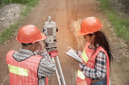 Surveyor or Engineer making measure by Theodolite with partner on the street in a field.の写真素材