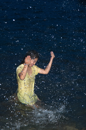 Happy pretty Asian woman open arms having fun in the sea playing with water splashes on tropical vacation at night.の写真素材