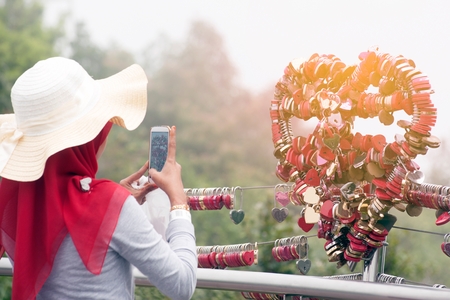 Asian woman take a photo by smart phone a Love padlocks by keys at Langkawi SkyCab, Malaysia.の写真素材