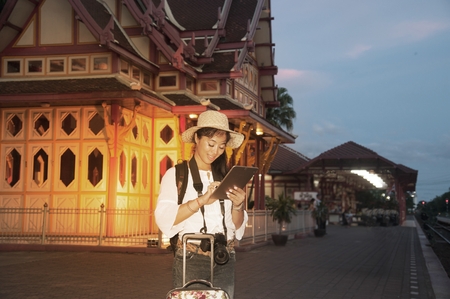 Pretty Asian traveler female looking tablet and waiting train at railway station in Thailand.の写真素材