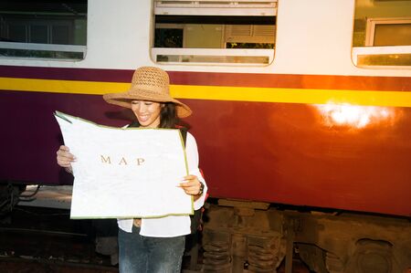 Pretty Asian traveler backpacker female looking map and waiting train at railway station in...