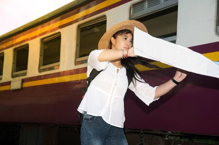Pretty Asian traveler backpacker female looking map and waiting train at railway station in Thailand.の写真素材