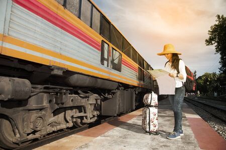 Pretty Asian traveler backpacker female looking map and waiting train at railway station in Thailand.の写真素材