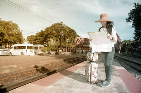 Pretty Asian traveler backpacker female looking map and waiting train at railway station in Thailand.の写真素材